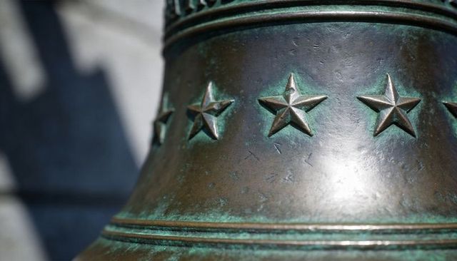 Featuring close-up sunlit bronze bell embossed with five-pointed stars and verdigris patina