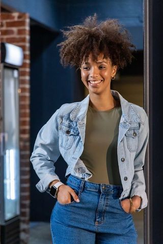 Smiling african american woman standing in retail entrance wearing denim jacket and jeans