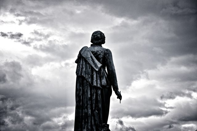 This powerful image depicts an ancient angel statue standing alone against a dramatic, cloud-filled sky. The dark, overcast clouds enhance the eerie and ethereal quality of the statue. Perfect for uses in themes of history, spirituality, melancholy, or dramatic landscapes. It can also be used in articles or presentations discussing religious symbols or ancient art.