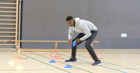 African american athlete training agility drill in gym using cones hurdles footwork markers