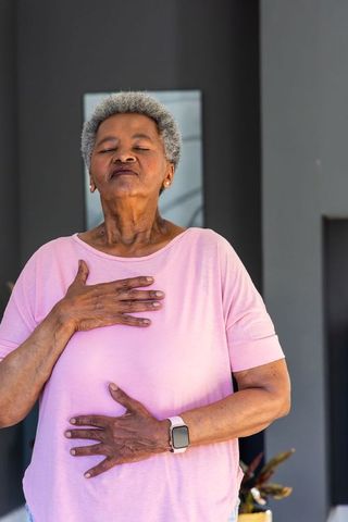 Senior african american woman practicing mindful breathing with hands on chest