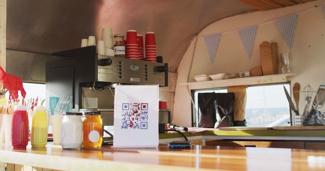 Food truck interior showcasing a coffee machine, condiments, jars, and a QR code menu on the counter. Ideal for advertising street food businesses, mobile dining experiences, and modern payment solutions. Shows a practical and inviting setup for customers.
