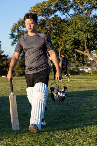 Young cricketer walking off field with bat and helmet during golden hour