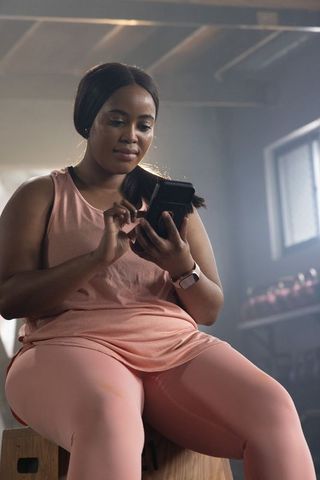 African american woman tapping phone on plyo box wearing pink activewear in gym studio