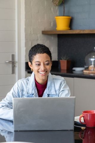 African american woman working remotely on laptop in kitchen workspace with coffee mug