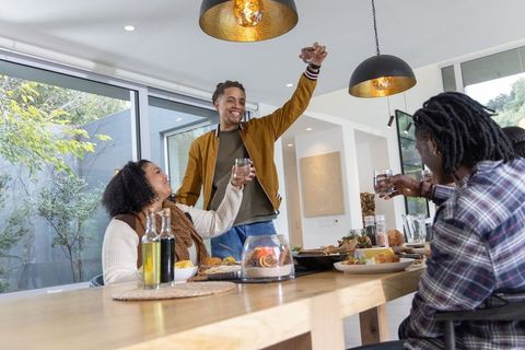Diverse friends toasting around long wooden dining table in modern open-plan home
