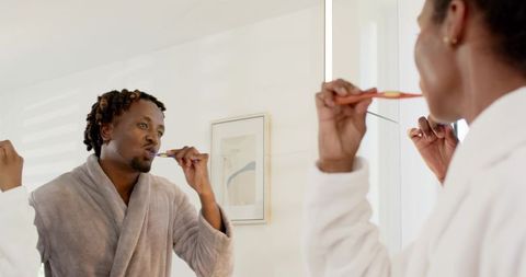 African american couple brushing teeth together in bright minimalist bathroom