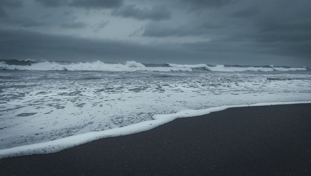 Moody stormy ocean shoreline with foamy waves sweeping dark wet sand under heavy clouds