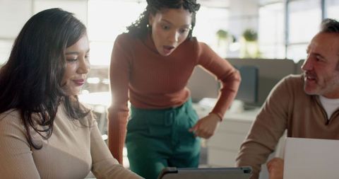 Diverse coworkers collaborating around tablet in bright modern office, surprised reaction