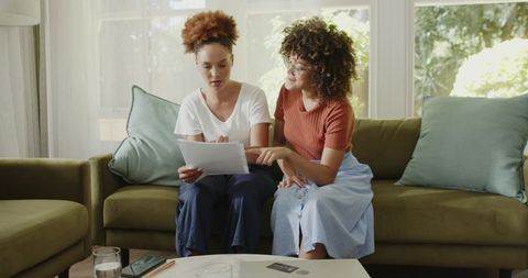Mid-adult women reviewing papers on sofa discussing finances and planning together