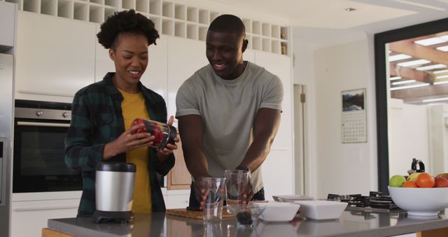 Image of happy african american couple preparing juice in kitchen. Love, relationship and spending quality time together concept.