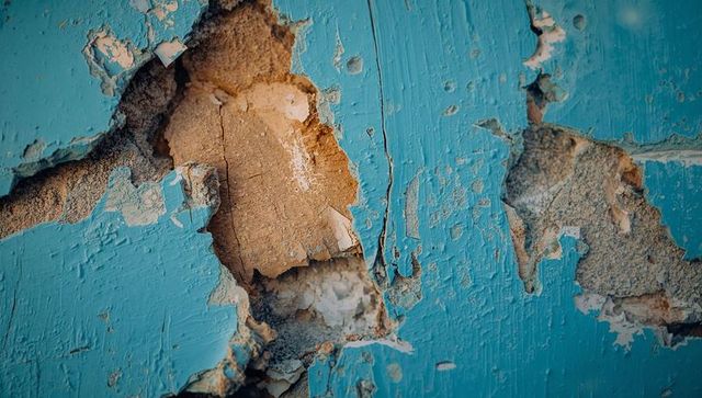 Peeling turquoise paint revealing weathered plaster texture, cracked masonry close-up