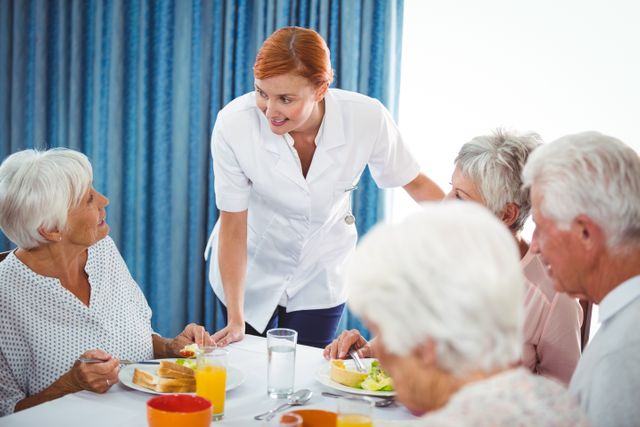Nurse engaging with senior residents during breakfast in a retirement home. Ideal for use in healthcare, elderly care, senior living, and community support contexts. Highlights the importance of interaction and care in senior living facilities.