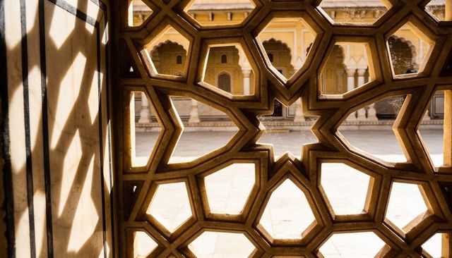 Sunlit sandstone jali lattice casting geometric star shadows across palace courtyard