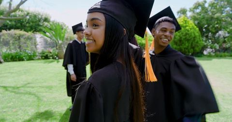 Smiling diverse graduates celebrating on campus lawn with bright orange tassels