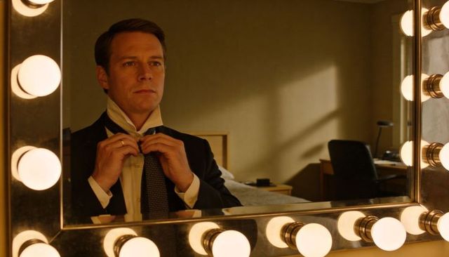 Man adjusting necktie in lighted vanity mirror in hotel room preparing for formal event
