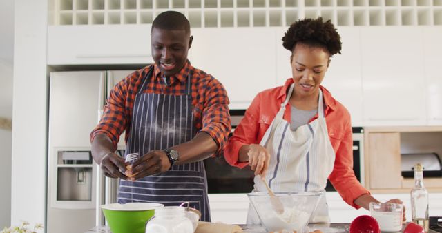 A joyful African American couple baking together in a cozy kitchen, displaying love and togetherness. Ideal for use in advertisements, articles, and blogs focusing on relationships, home activities, culinary arts, and family bonding. This image could be used to promote cooking classes, relationship counseling, or kitchenware. Suitable for websites, social media posts, and magazine covers emphasizing the importance of spending quality time with loved ones.