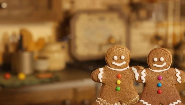 Smiling Gingerbread Couple Decorating Holiday Kitchen Tabletop with Candy Buttons and Icing
