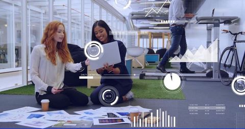 Women collaborating on laptop and charts in modern coworking office with treadmill