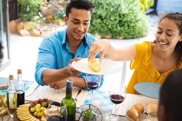 Friends enjoying a sunny outdoor brunch, serving food to each other at a table on a patio. Ideal for use in lifestyle blogs, social media posts about gatherings, food and drink advertisements, and articles promoting social activities and outdoor dining.