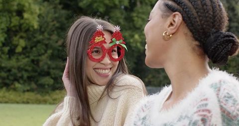 Friends laughing wearing red glitter christmas-tree glasses and cozy sweaters outdoors