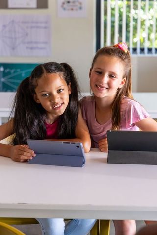 Diverse elementary school girls using tablets in classroom smiling and collaborating