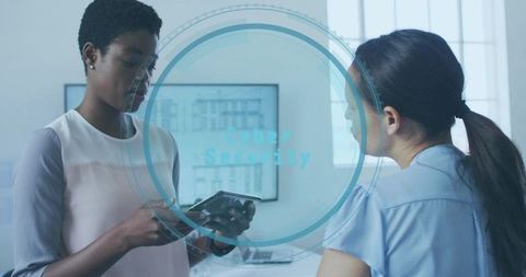 Women reviewing tablet with cybersecurity hud in modern office collaborating on security