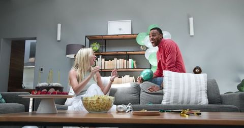 Cheerful couple preparing for celebration with balloons and treats