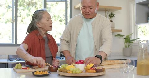 Senior couple preparing colorful fruit platter on kitchen island for casual brunch