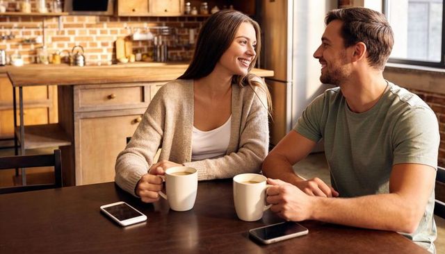 Couple sharing morning coffee, smiling and chatting at cozy kitchen table