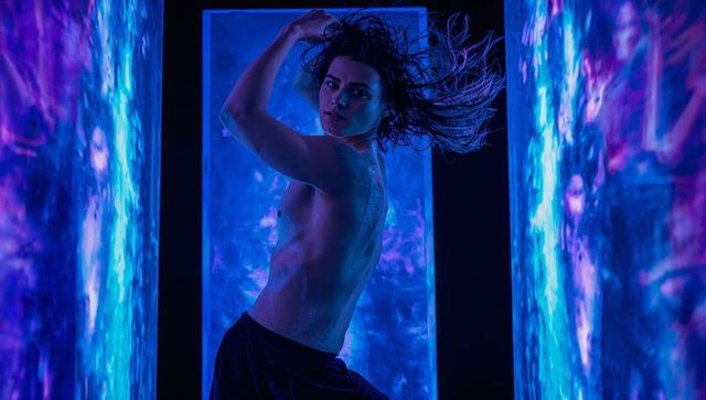 Shirtless male dancer tossing hair between neon cyan panels wet skin dynamic motion