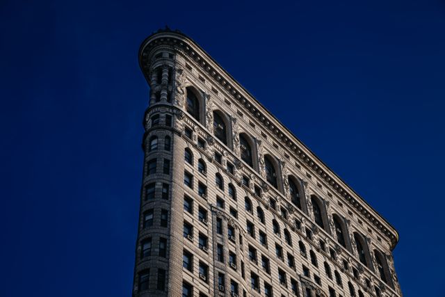 Picture shows the iconic Flatiron Building against a clear blue sky in New York City. Great for promoting travel to NYC, architectural studies, urban landscapes, or as an element in marketing materials highlighting historic and famous landmarks of the city.