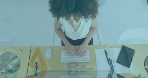 Overhead view showing woman typing at wooden desk with tablet, notebook and glasses