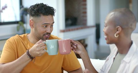 African american couple clinking coffee mugs on cozy sofa by fireplace sharing joy