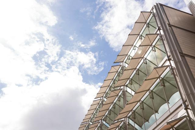 Low angle view of a modern building exterior featuring canopy windows against a blue sky with clouds. Ideal for use in architectural design presentations, urban development projects, and real estate marketing materials.