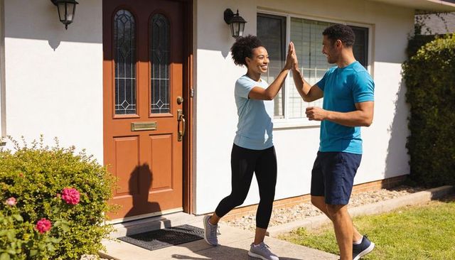 High-fiving couple celebrating outdoor workout on sunny suburban front walkway