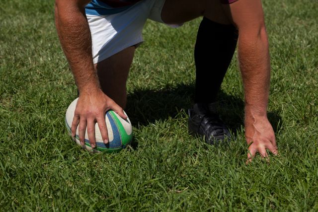 Low section of player crouching with rugby ball on field