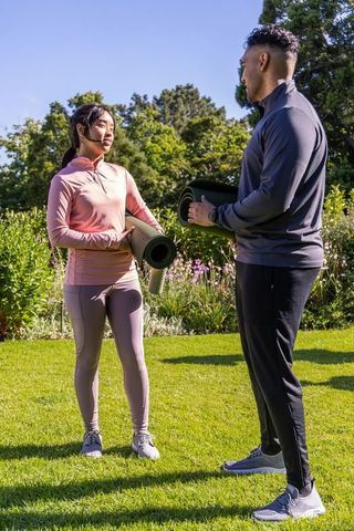 Asian woman and african american man chatting with yoga mats on sunny park lawn