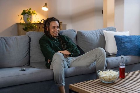 African american man relaxing on gray sofa watching movie with popcorn in cozy room
