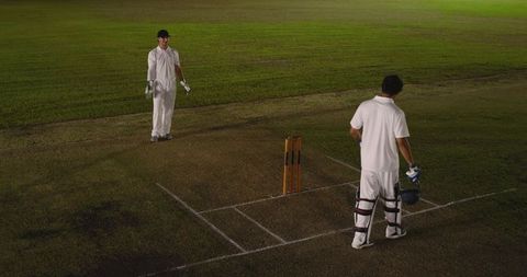 Floodlit night cricket: batsman and wicketkeeper standing at crease by stumps