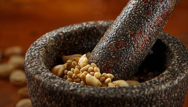 Grinding peanuts in speckled granite mortar and pestle closeup rustic kitchen texture