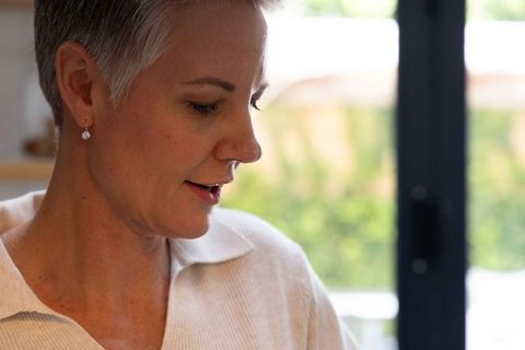 Mature woman reading aloud by window, short gray hair, pearl earring, natural light