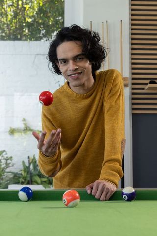 Young man tossing red billiard ball on green pool table in cozy home game room