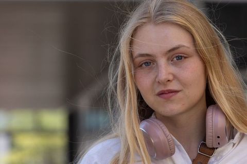 Young woman wearing pink headphones on urban street portrait with natural breeze