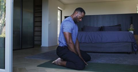 Man practicing kneeling breathwork and gentle stretching on yoga mat in minimalist bedroom