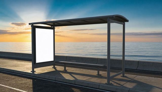 Coastal bus shelter casting long shadows at sunset with blank advertising panel and bench