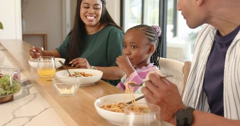 Diverse family sharing spaghetti meal at sunlit modern open-plan kitchen counter