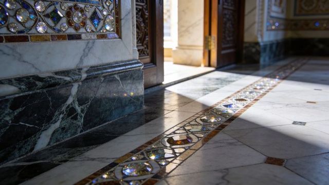 Sunlit gemstone mosaic inlay on polished marble floor in ornate grand hall corridor