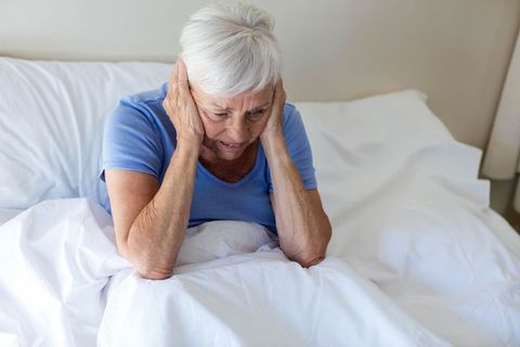 Elderly Woman Sitting on Bed with Hands on Head