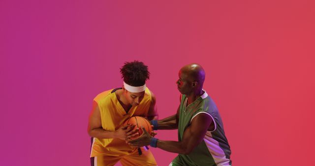 Image of two diverse male basketball players playing with ball on pink background. Sports and competition concept.